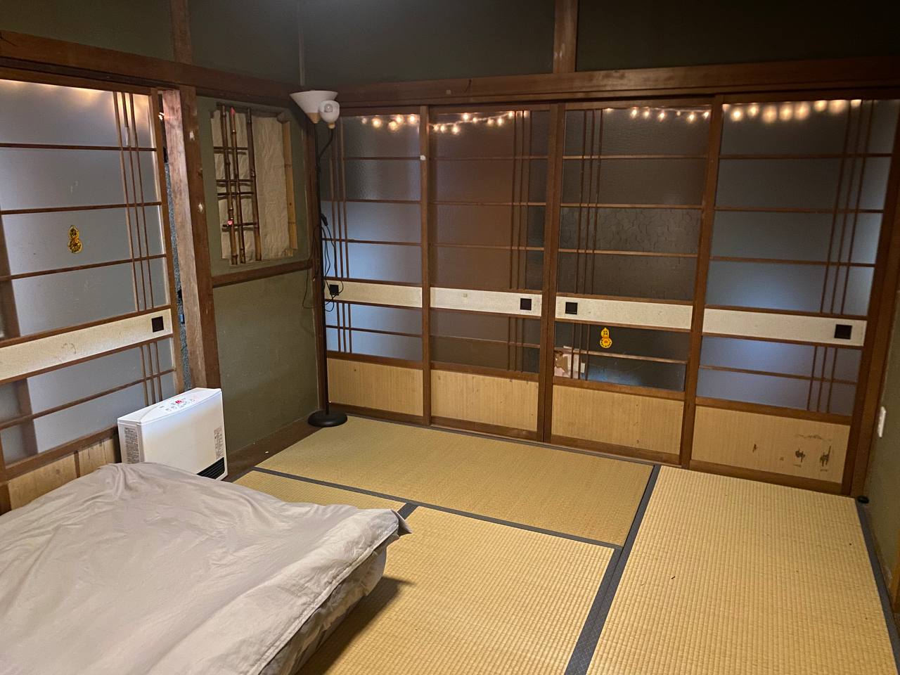 A tatami room at the Kaizen Dojo with sliding shoji screens along one wall, exposed dark timber posts and beams, and warm string lights.