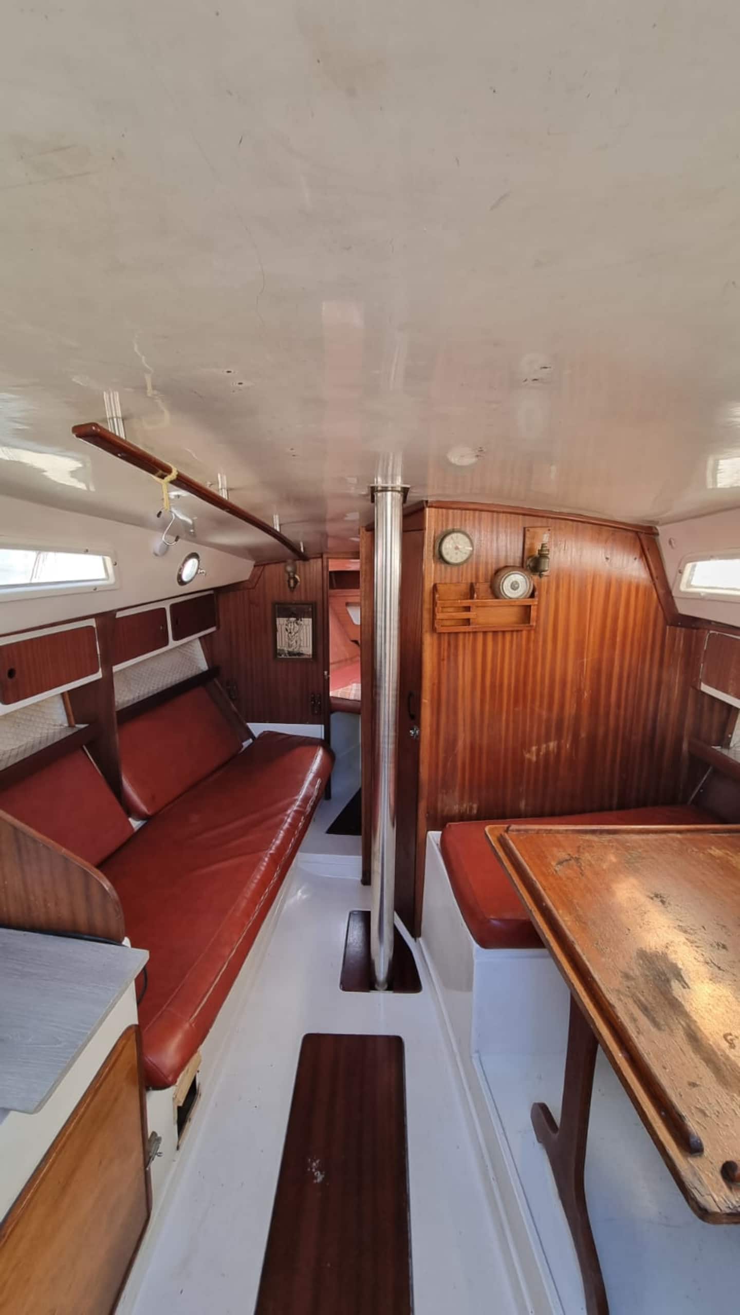 The saloon of the Monaco sailboat: varnished mahogany joinery, red bench berths either side, and brass instruments on the bulkhead.